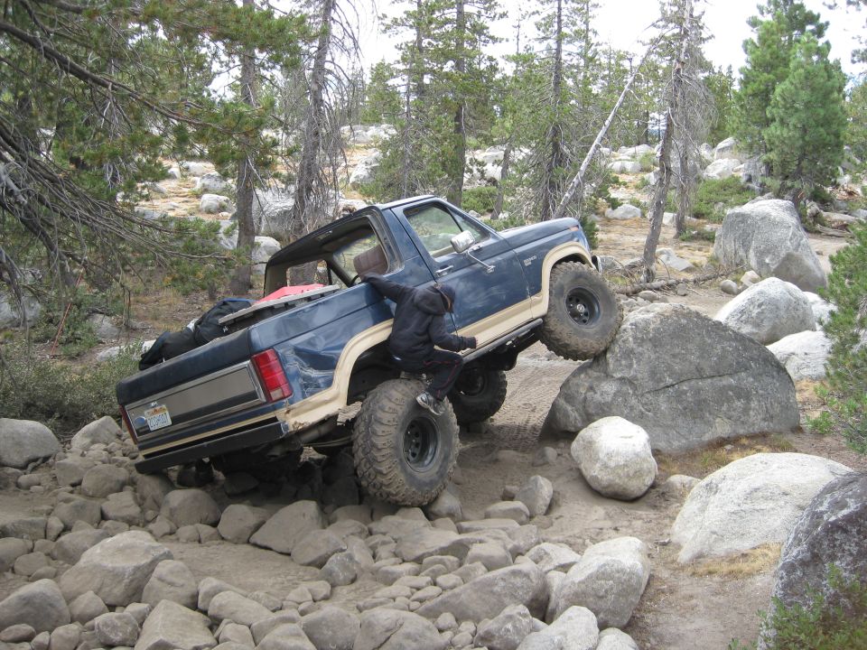 Blue 1980s Ford Bronco climbing large rocks on a trail