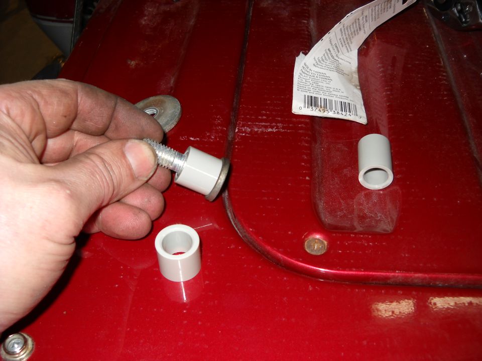 Hand holding a bolt with a white sleeve and washer, next to other parts on a red surface