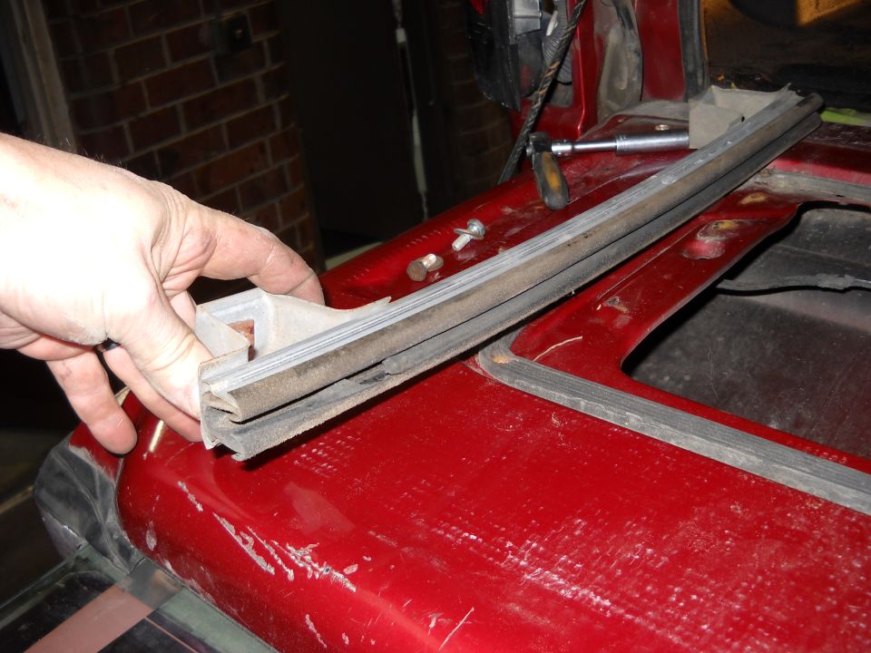 Hand holding a rubber window seal strip over a red vehicle body panel