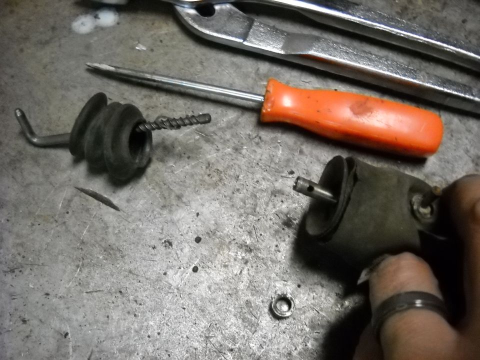 Automotive part, possibly a vacuum actuator, next to a screwdriver and pliers on a metal workbench