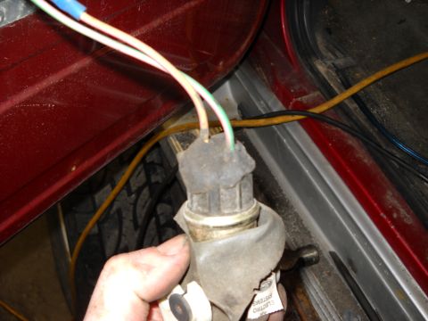 1993 Ford C-150 (Centurion Conversions) - Close-up of a door lock actuator and its wiring harness, with a red interior panel and tire in the background.