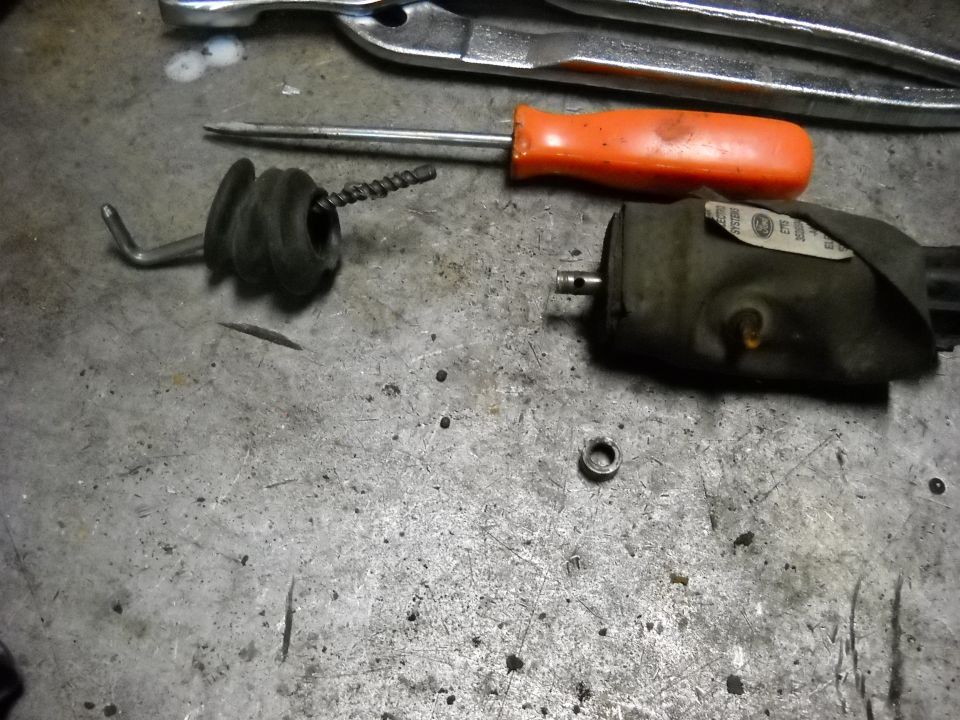 Door lock actuator with rubber boot and metal rod, screwdriver, and pliers on a workbench