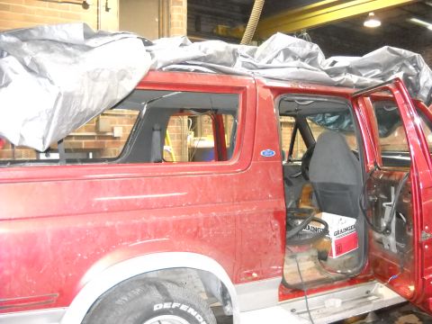 1993 Ford C-150 (Centurion Conversions) - The interior of a red SUV is visible with the doors open and a tarp covering the roof.