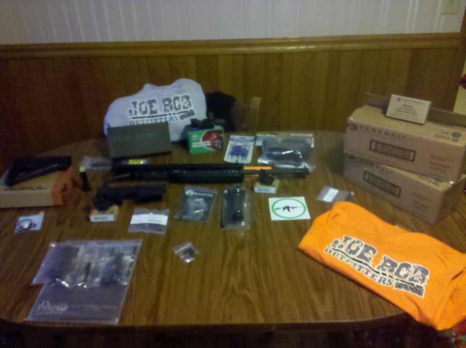 Table covered with AR rifle parts, ammo boxes and Joe Bob Outfitters shirts