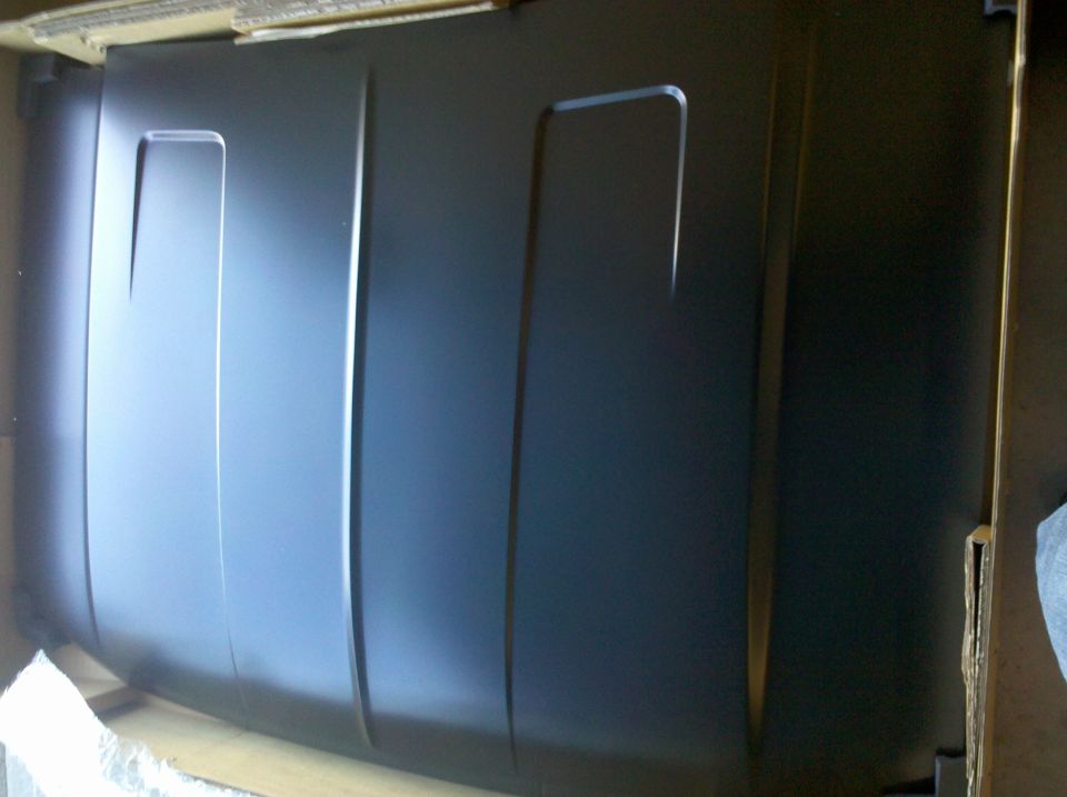 New black primered steel hood panel in its cardboard shipping crate
