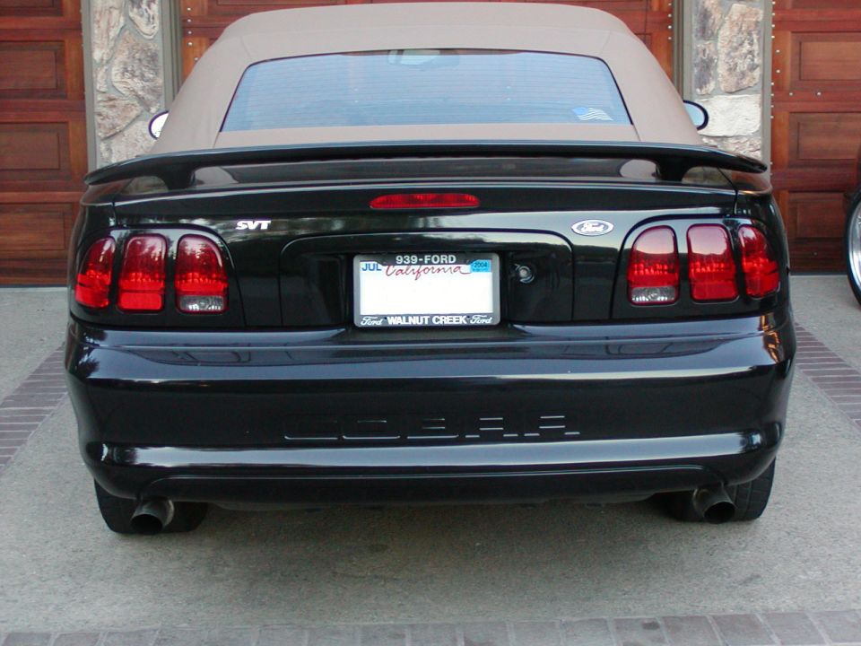 Black convertible Mustang SVT Cobra parked in front of a garage door. Has a tan top and a California license plate