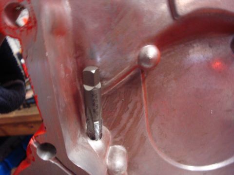 1989 Ford Bronco - A tap tool is inserted into a red engine component, with bolt heads visible on the surface.