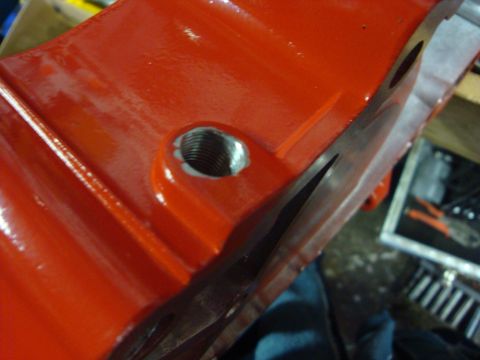 1989 Ford Bronco - Close-up view of a red engine component, possibly a valve cover or oil pan, showing a threaded opening and machined surfaces.