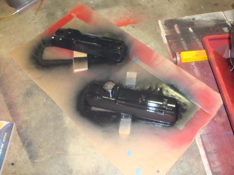 1989 Ford Bronco - Two freshly painted black valve covers are drying on a drop cloth, ready for installation.