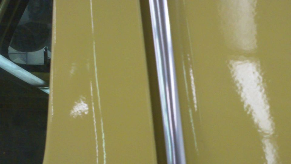 Yellow car door with chrome trim strip, showing reflections and minor paint imperfections