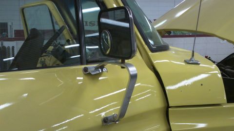 1978 Ford Bronco - Close-up of a yellow truck's side door and mirror, with the hood open revealing the engine bay.