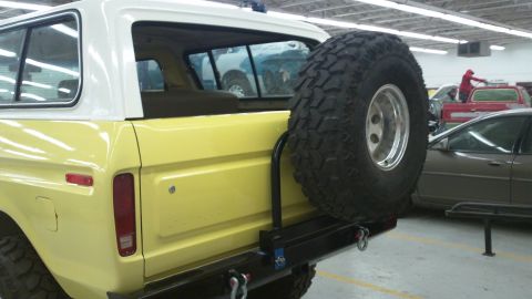 1978 Ford Bronco - Rear view of a yellow 1978 Ford Bronco, showing the spare tire and other vehicles in the background.