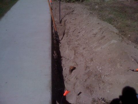 1968 Ford Mustang - Trenching work is underway next to a sidewalk, with orange markers indicating underground utilities.