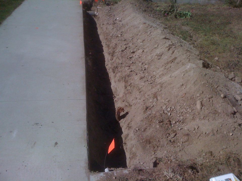 Trench dug next to a concrete sidewalk with orange flags marking the area