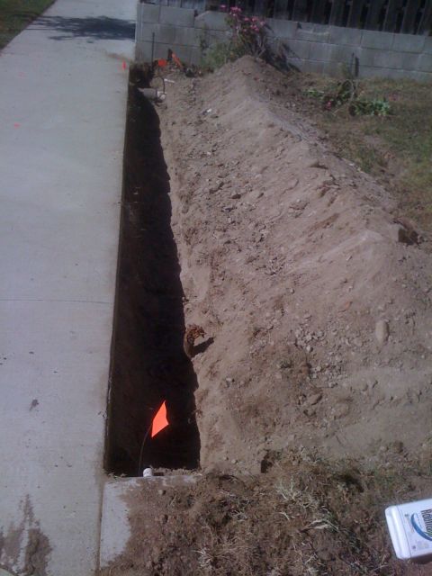 1968 Ford Mustang - A deep trench has been excavated alongside a concrete sidewalk, with orange flags indicating the work zone.