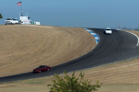 1997 Ford Taurus - Two cars race on a track with dry grass and a flag stand in the background.