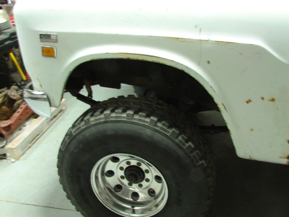 Close-up of a white International pickup truck's front fender and large tire. Badge reads '100'