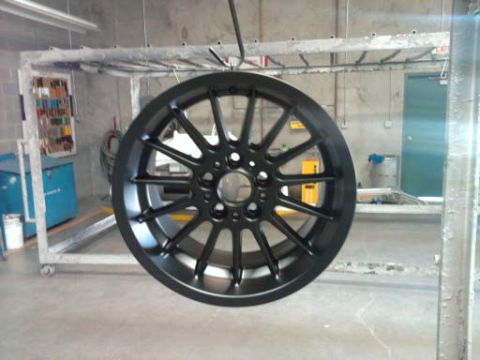 1994 Ford F-150 - A black aftermarket wheel is shown hanging in a workshop, likely during a powder coating process.