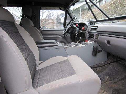 1996 Ford Bronco - The interior of a truck shows grey seats, a roll cage, and a modified center console.
