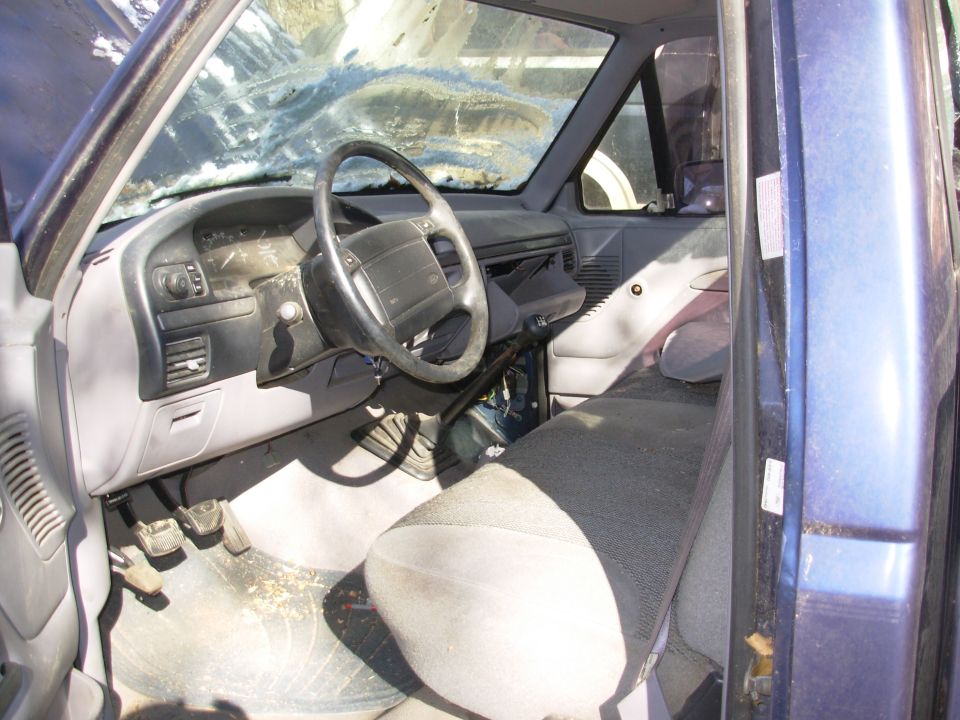 Interior of an older Ford truck cab with cloth bench seat and manual pedals