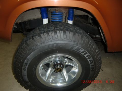 1973 Ford Bronco - Close-up of an orange SUV's wheel well, bright blue shocks and an off-road tire with visible tread detail.