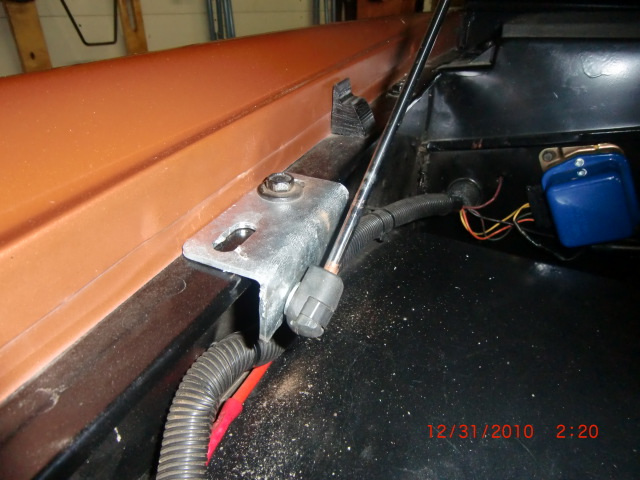 Orange vehicle hood edge with metal bracket and black wiring harness