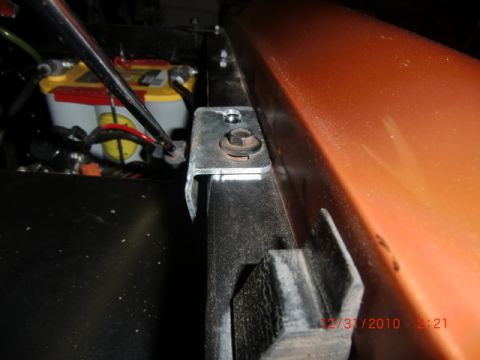 1973 Ford Bronco - Close-up of a car battery and its mounting bracket, with part of the vehicle's orange body visible.