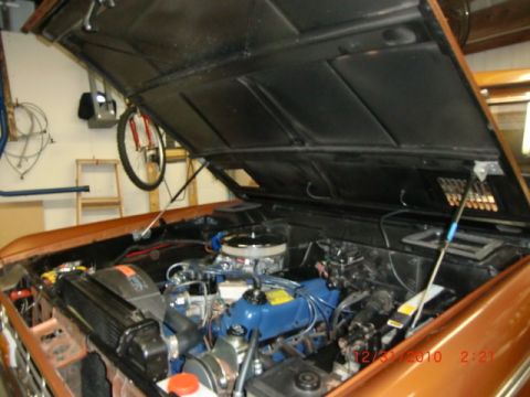 1973 Ford Bronco - The engine compartment of an older vehicle is shown with the hood raised, revealing the motor and surrounding components.