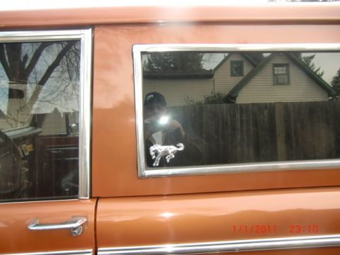 1973 Ford Bronco - A chrome horse emblem is visible on the side window of an orange SUV, with a reflection of the photographer in the glass.