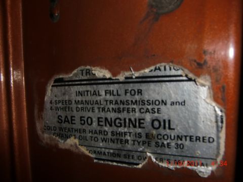 1973 Ford Bronco - A close-up view of a torn sticker detailing initial fill specifications for a 4-speed manual transmission and transfer case.