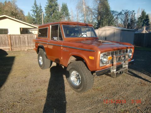 1973 Ford Bronco - This orange SUV is parked in a residential driveway with a house and fence in the background.