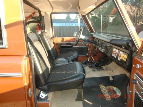 1973 Ford Bronco - The interior of a 1973 Ford Bronco features black seats, a dashboard with various controls, and branded floor mats.