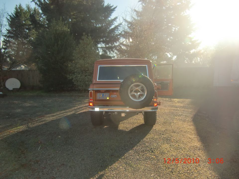 Orange Ford Bronco with spare tire on rear, driver's door open, seen from behind