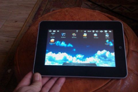 1991 Ford LTD Crown Victoria - A tablet computer is held in a hand, resting on a textured surface, with its screen showing a cloud-filled sky wallpaper.