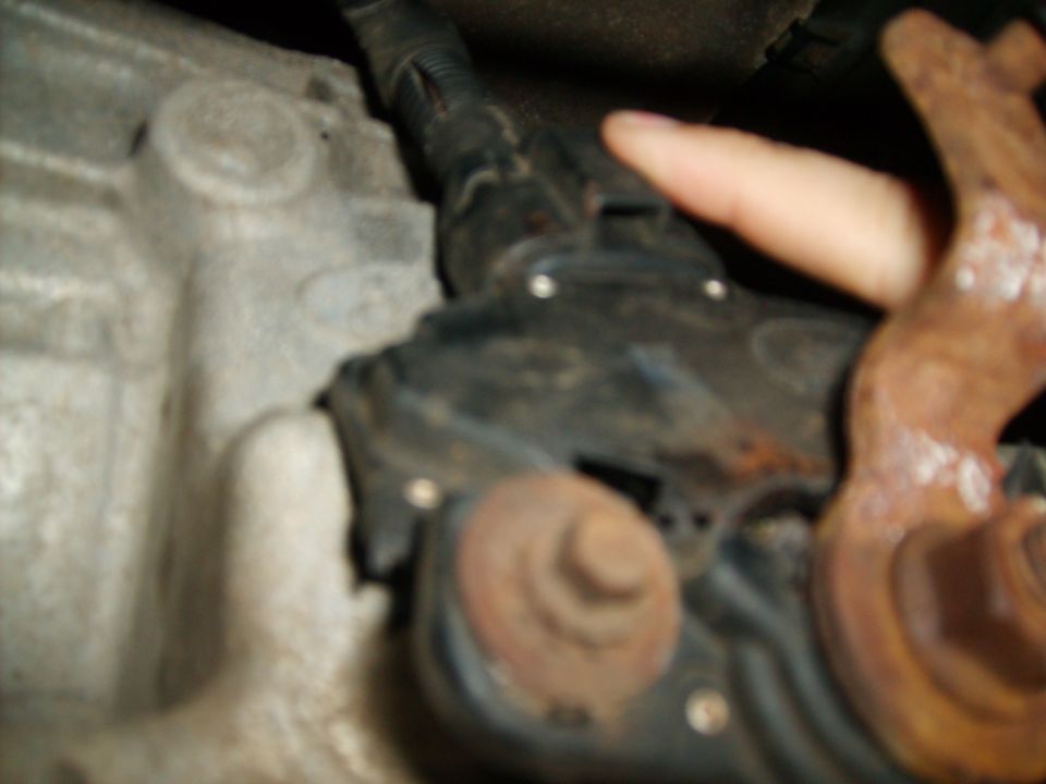 Close-up of a vehicle's transmission area with a finger pointing to a black component