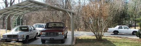 1985 Ford Crown Victoria LTD - A white sedan is seen parked on the side of the road, with other vehicles visible under a carport.