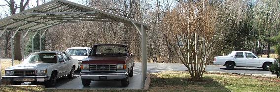 White Ford sedan and maroon two-tone Ford pickup parked under a metal carport in winter