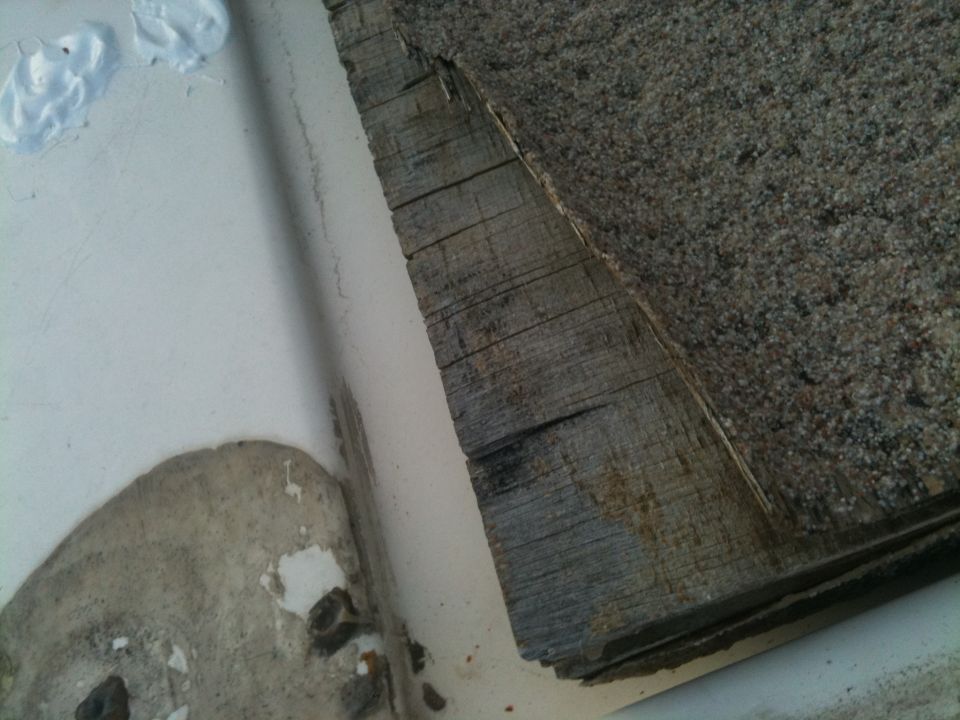 Weathered wooden planks with asphalt shingles next to a white curved surface with peeling paint and dark spots