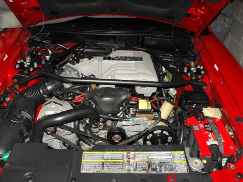 1994 Ford Bronco - The engine bay of a red vehicle, a V8 engine, air intake system, and a red battery. Text is visible on the engine cover and under the hood.