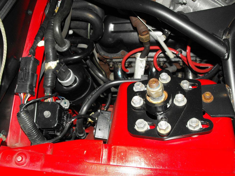 Engine bay with red painted metal, black hoses, wiring, and a black metal bracket with bolts