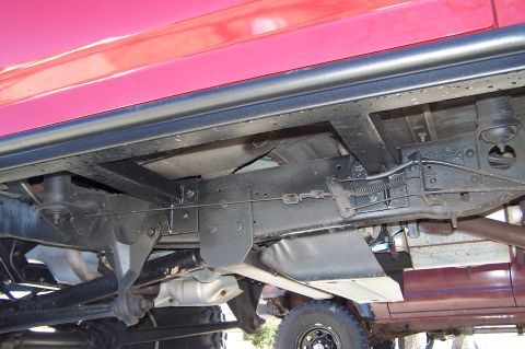 1990 Ford Bronco - This image shows the underside of a red vehicle, focusing on the frame, suspension, and exhaust system. No specific year or model is identi…