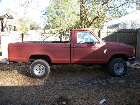 1994 Ford Explorer - A red pickup truck is parked outdoors on a dirt lot, showing its side profile with aftermarket wheels.