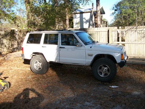 1994 Ford Explorer - A white Jeep Cherokee is parked outdoors, showing its side profile with off-road tires and aftermarket wheels.