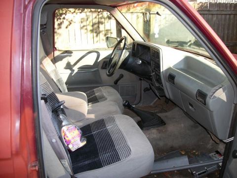 1994 Ford Explorer - The interior of a vehicle shows worn seats and a cluttered dashboard with a spray bottle on the passenger seat.