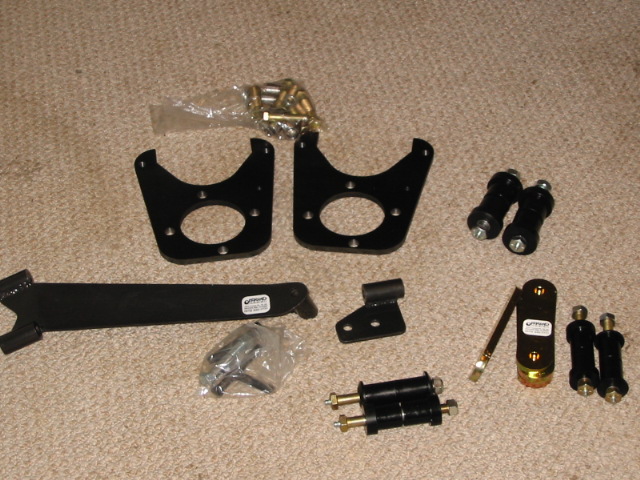 Brake bracket kit and hardware laid out on carpet, including black caliper brackets, end links, and plated bolts