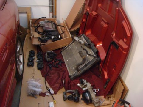 2001 Pontiac Trans Am - Various engine components and a red car hood are laid out on a garage floor.
