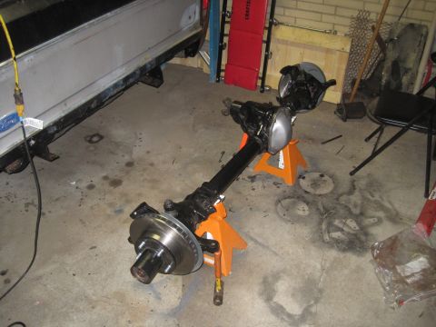 1979 Ford Bronco - Front axle assembly with disc brakes is supported by jack stands in a garage setting.