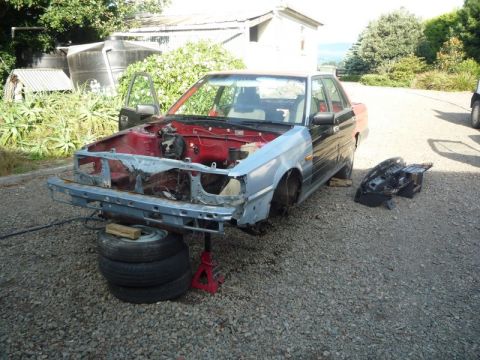 1969 MINI Cooper - A car sits disassembled in a gravel lot with its front end removed and hood open.