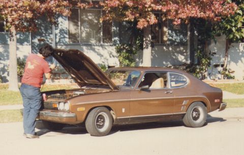 1968 Ford Mustang - Person working on the engine of a brown 1974 Ford Capri II coupe parked on a street.