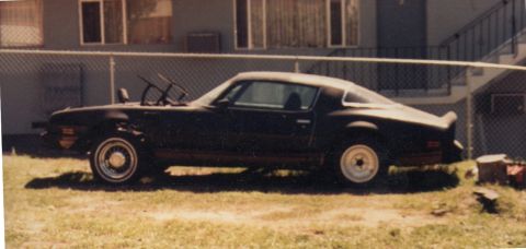 1968 Ford Mustang - A dark-colored coupe with a spoiler and damaged front end is parked on grass.